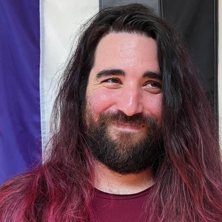 A picture of my smiling face, standing in front of an asexual pride flag